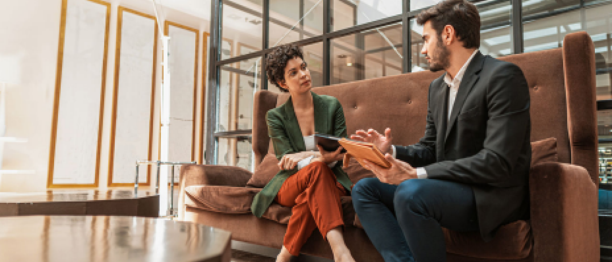 Twee professionals die een geconcentreerd gesprek voeren terwijl ze in een moderne kantoorhal zitten.