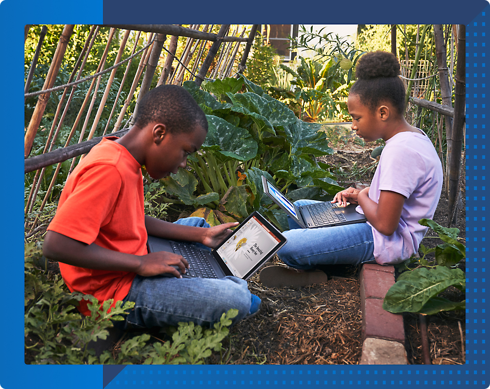 A boy and girl sitting in a garden using laptops.