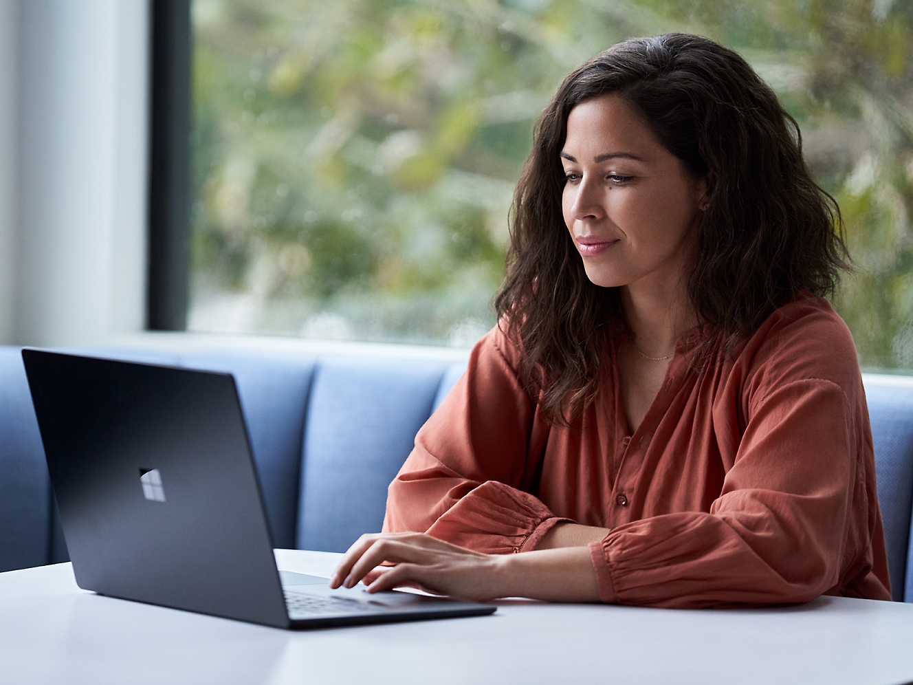 Een vrouw die aan een tafel zit en een laptop gebruikt.
