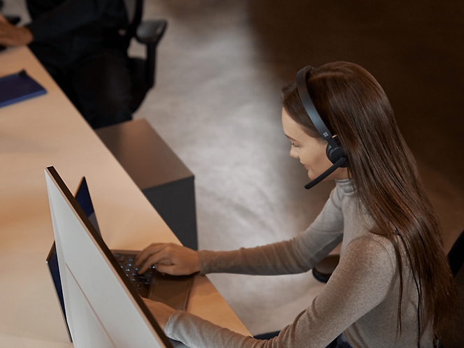 Een vrouw die een headset draagt terwijl ze op een laptop werkt.