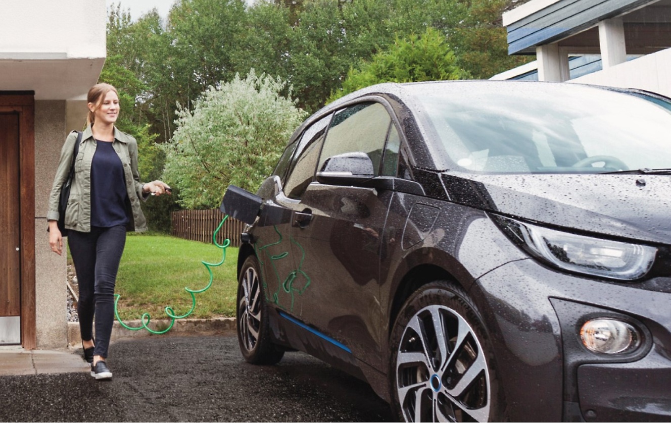 一位女士在一所房子前給 BMW i3 充電。