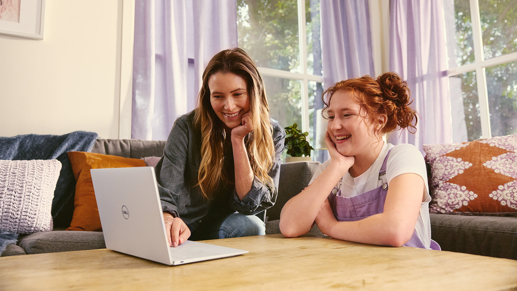 An adult and a young person sit in a living room using a laptop together.
