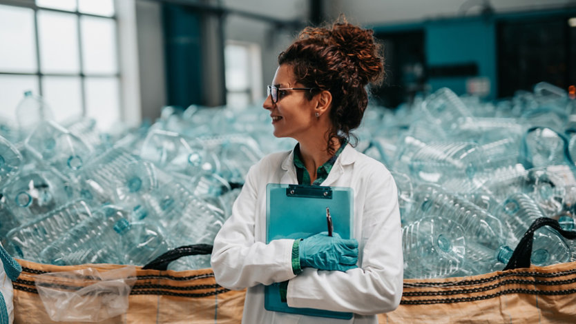 Woman standing in front of bin full of empty plastic bottles.