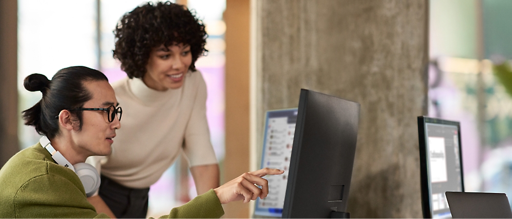 Two people working together at a computer, both focused on the display.
