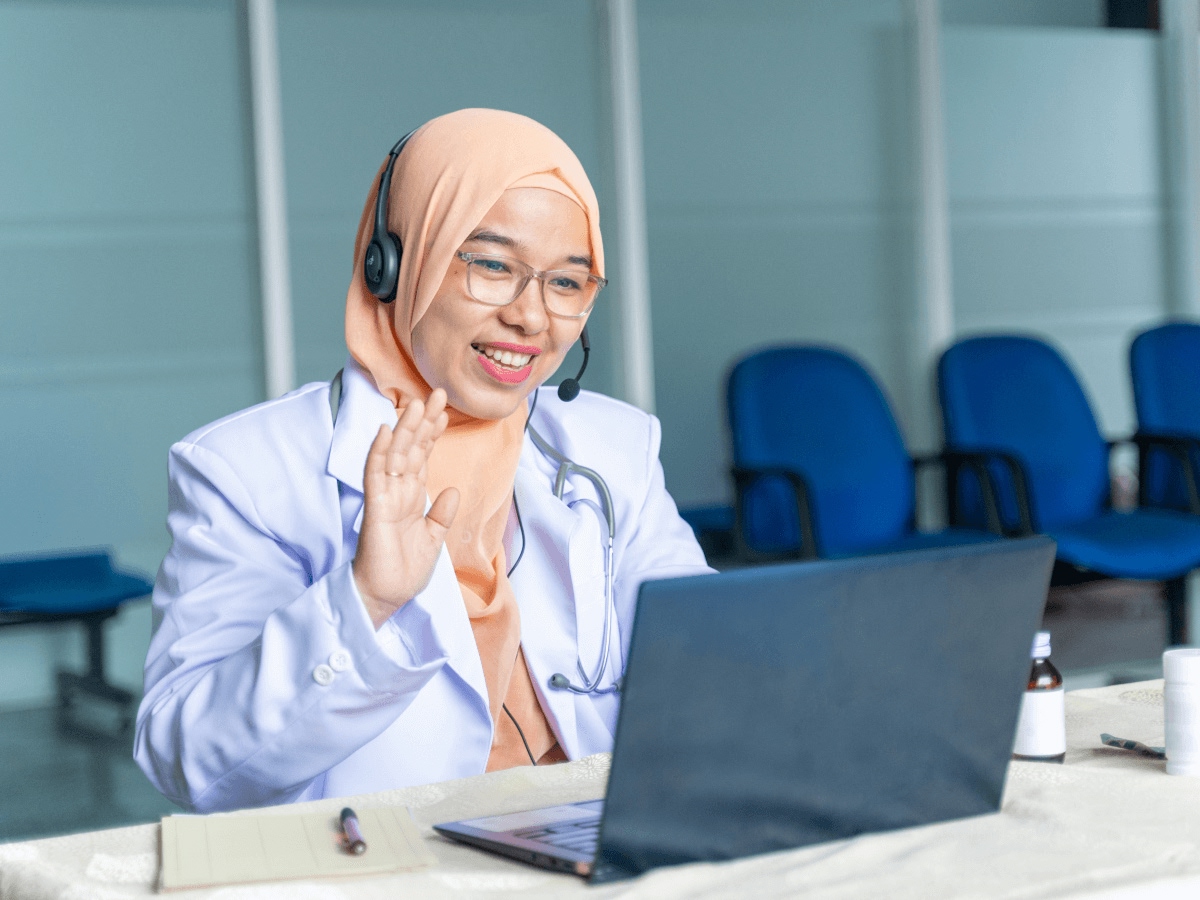 Woman with headset on waving at laptop