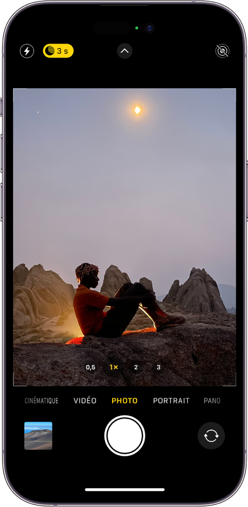 L’écran « Appareil photo » en mode Photo. Les boutons correspondant au flash et au mode Nuit s’affichent dans l’angle supérieur gauche de l’écran et le mode Nuit est activé. Le bouton « Commandes de l’appareil photo » se trouve en haut au centre et le bouton « Live Photo » dans le coin supérieur droit. En bas de l’écran, de gauche à droite, se trouvent le bouton « Visualiseur de photos et vidéos », le bouton « Prendre une photo » et le bouton « Sélecteur de caméra - face arrière ». Une scène de nuit apparaît dans le cadre de l’appareil photo.