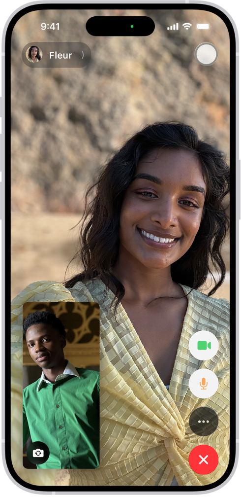 Obrazovka FaceTime s prebiehajúcim hovorom. V hornej časti obrazovky je zobrazené meno účastníka na väčšom obrázku. Obrázky ostatných účastníkov sa zobrazujú v malom obdĺžniku vľavo dole spolu s tlačidlom Otočiť kameru. Obrázky ostatných účastníkov sa zobrazujú v dlaždiciach nad ním. Vpravo dole na obrazovke sú ďalšie ovládacie prvky FaceTime: Tlačidlá Kamera, Mikrofón, Viac a Ukončiť hovor.