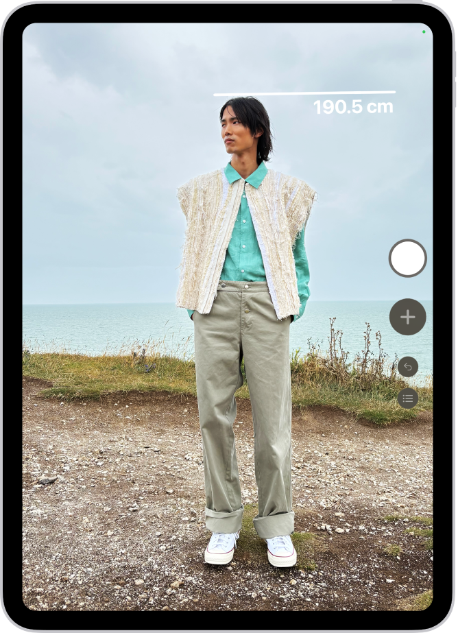 “测距仪” App 中正在测量一个人的身高,身高测量值显示在此人头顶。右下角附近的“拍照”按钮用于给测量结果拍照。绿色“相机使用中”指示器显示在顶部。