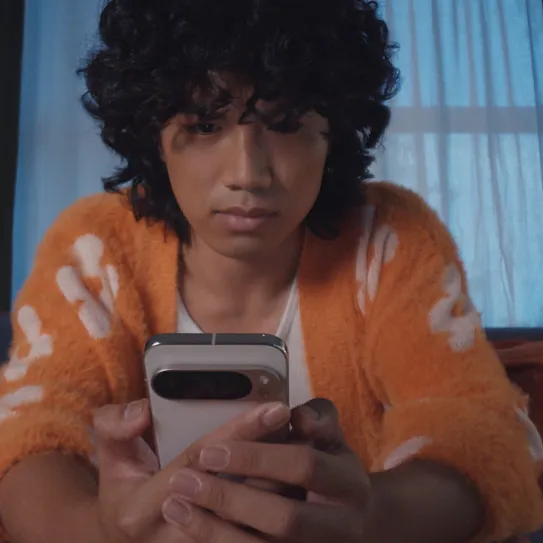 A person wearing an orange and white cardigan sits and looks at their Pixel phone.